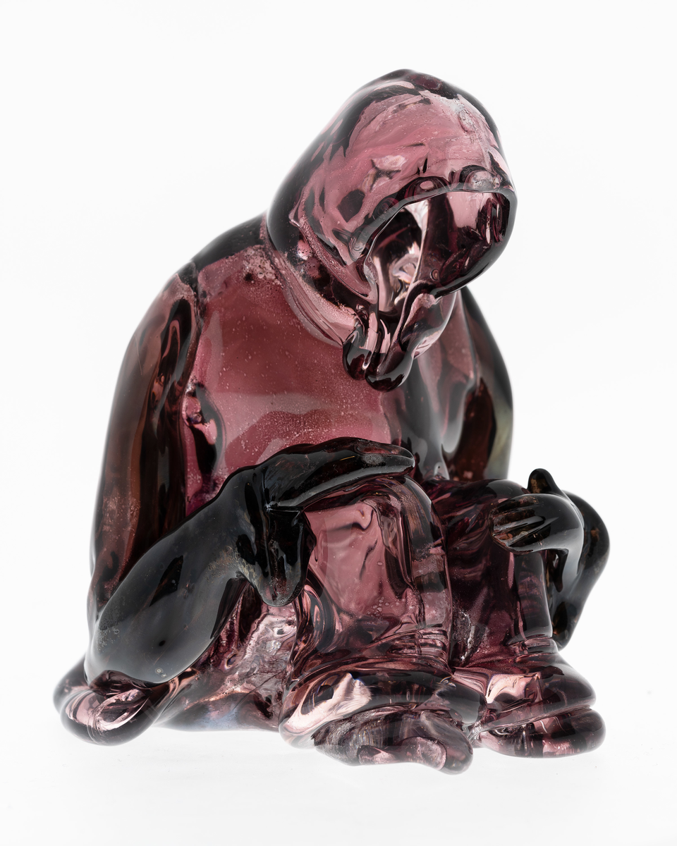 Skulptur i gjennomskinnelig lillafarget glass, i form av en sittende hettekledd skikkelse.