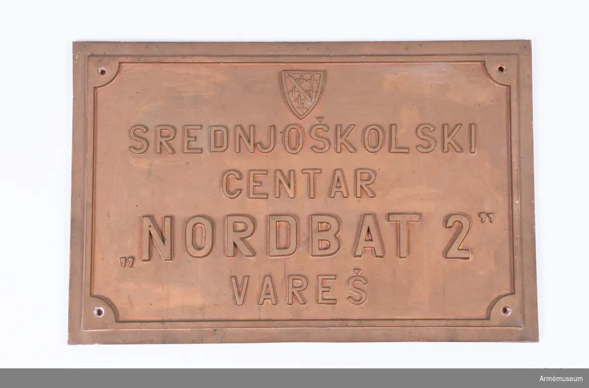 Metallplatta med inskription som varit fäst på insidan av ett fönster på gymnasieskolan Goran Kovacic i Vares i Bosnien. Under 1994 döptes skolan om till ”Nordbat 2” efter de händelser som tidigare tilldrog sig i och omkring skolan där delar av den svensk-danska pansarskyttebataljonen som ingick i UNPROFOR befann sig. Nordbat 2 ingick i BA01 som var den första av de svenska bosnienbataljonerna för de fredsbevarande styrkorna. 

På baksidan av plattan återfinns inskriptioner från elever på skolan. Föremålet förmedlades genom överste Ulf Henricsson och Stig-Inge Blennow.