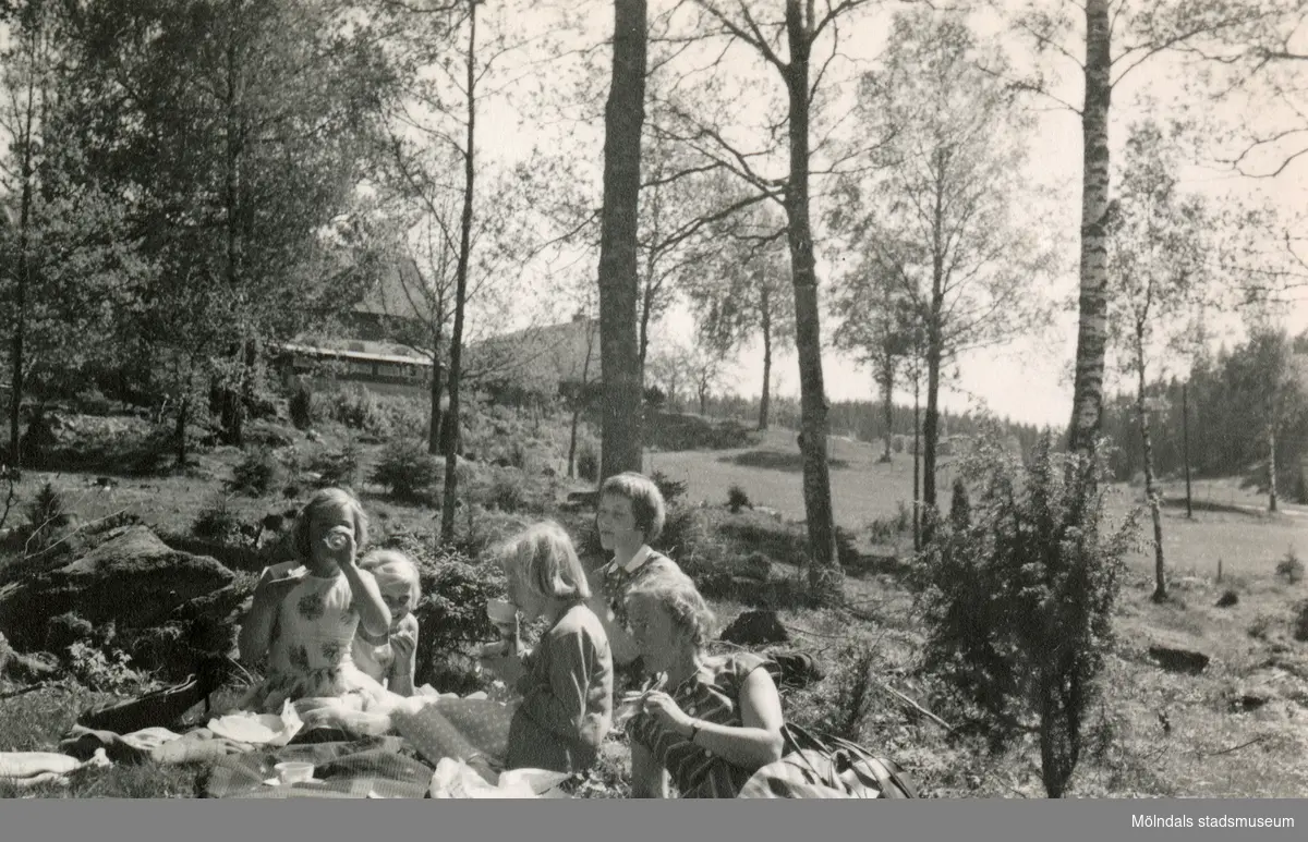 Rosa Pettersson (född Krantz), dottern Eva (gift Kempe) och hennes lekkamrater Lena Englund och Monika Axelsson har picknick i det gröna efter att flickorna har kastat varpa, Insered i Hällingsjö 1957. Relaterat motiv: 2023_0154.