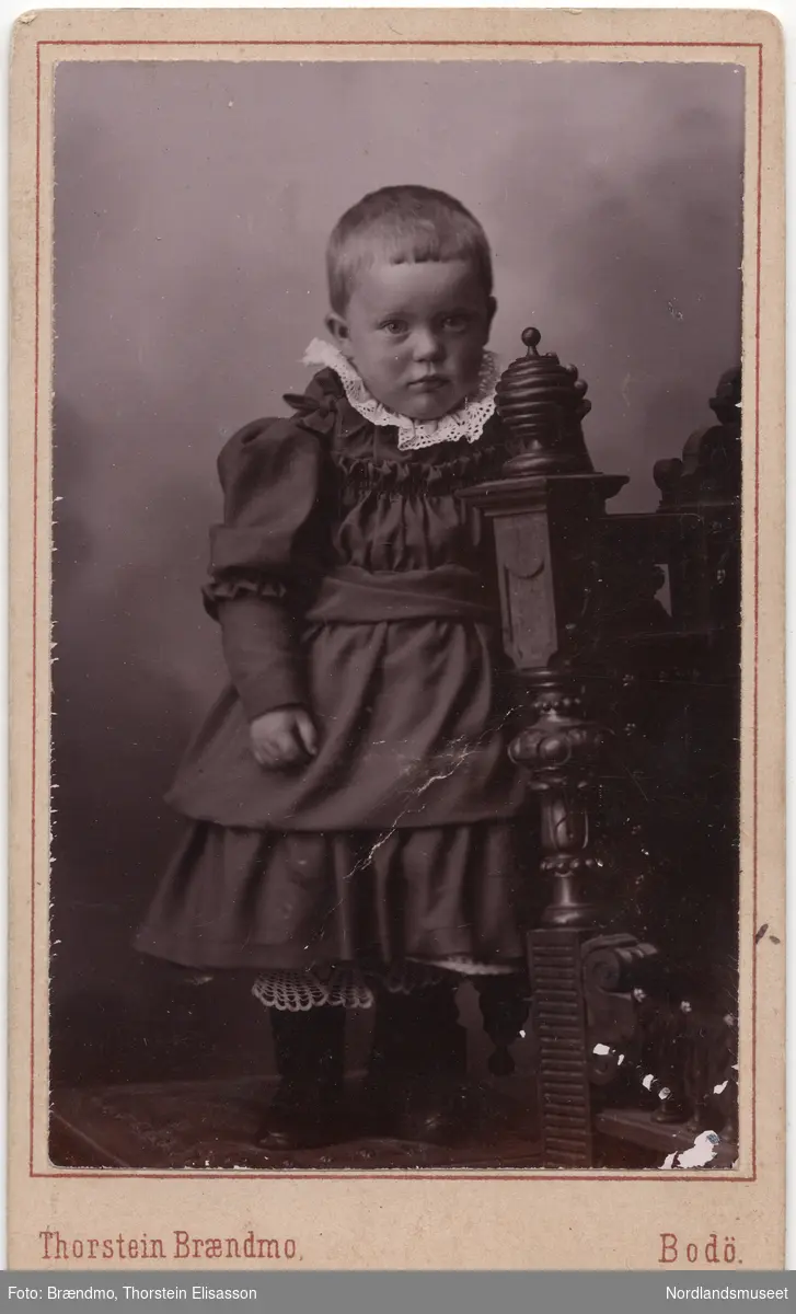 Portrettbilde av en liten jente i kjole. Gerda Marie Fremmerlid. Helfigur. Atelierbilde.