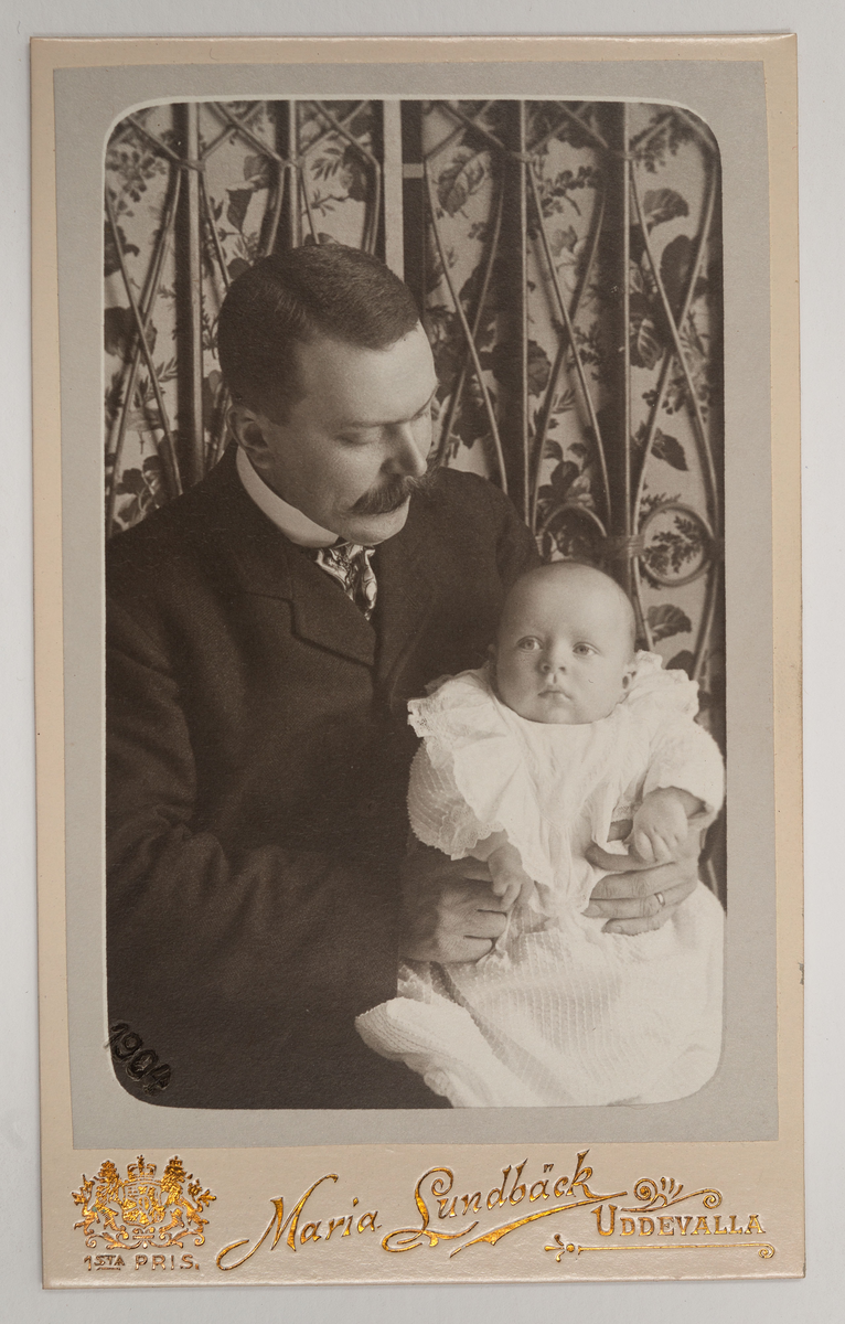 Visitkortsporträtt av Anders Zachau med son. Fotografiet sitter i fotoalbum som tillhört Gertrud Zachau. Fotografiet sitter på sida 25.