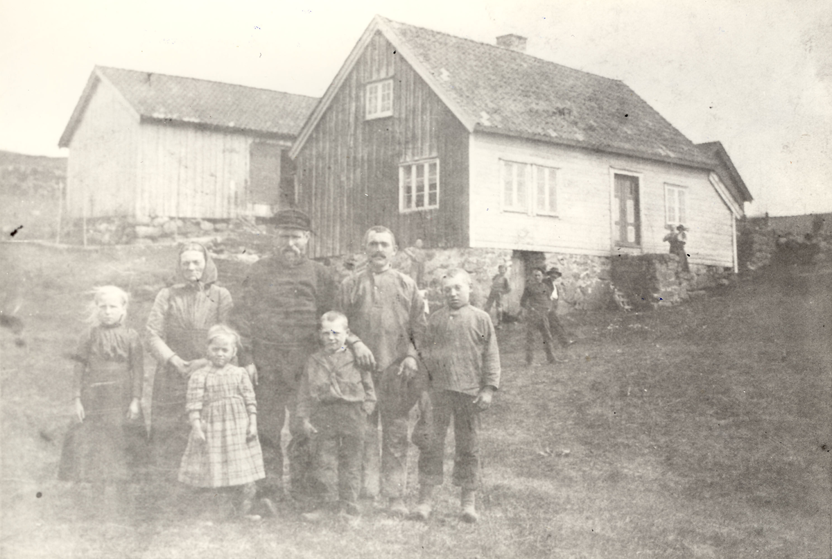 Familien Martin Larsen Stapnes samlet foran bolighuset på gården på Stapnes, i bakgrunnen står noen ukjente personer