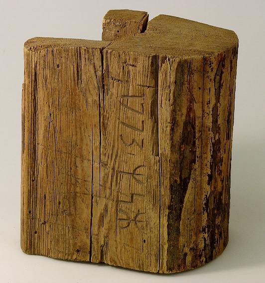 Ett stycke av en övre DÖRRSTOCK till ett fähus. Skuret i trä 1773 samt ett bomärke om tre tecken, runor.