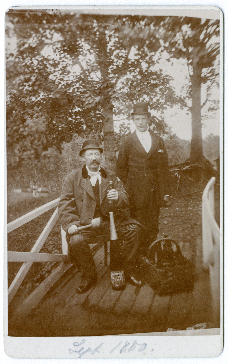Foto av kommandør Niels Juel (sittende) og ukjent mann ved siden av. Foto tatt i 1880, antagelig på Dal gård.

Juel ser ut til å holde på sportutstyr av noe slag og en stråkurv med flasker står ved siden av.
