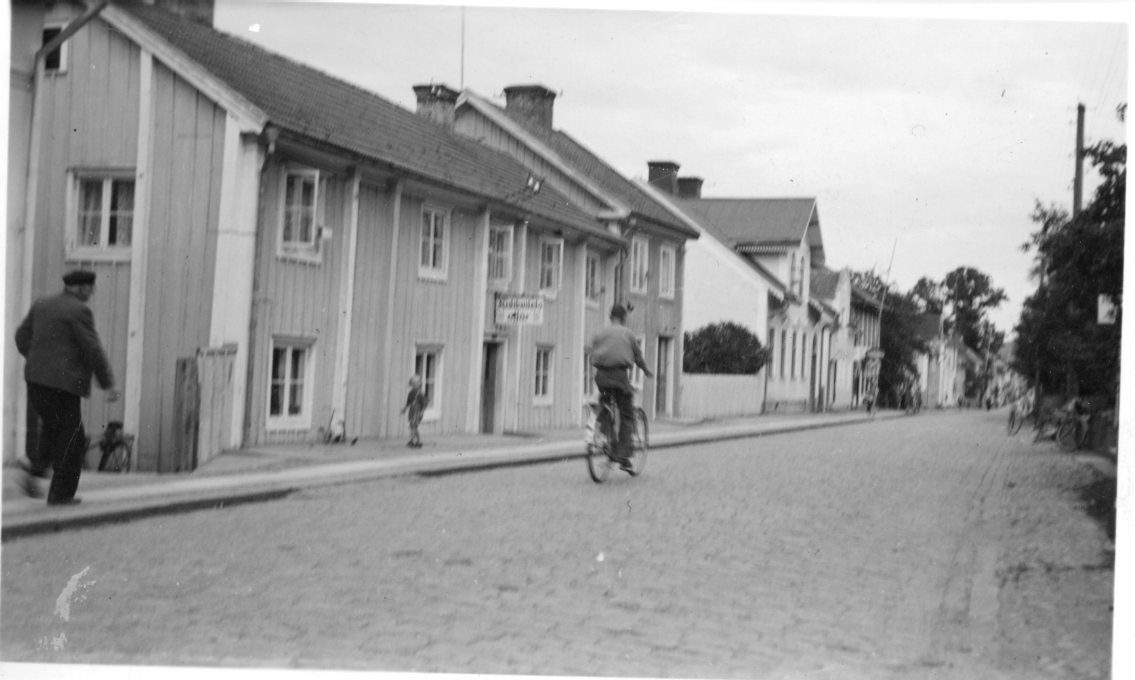 En man cyklar norrut på Brahegatan. En äldre man går på trottoaren, möter en liten pojk.