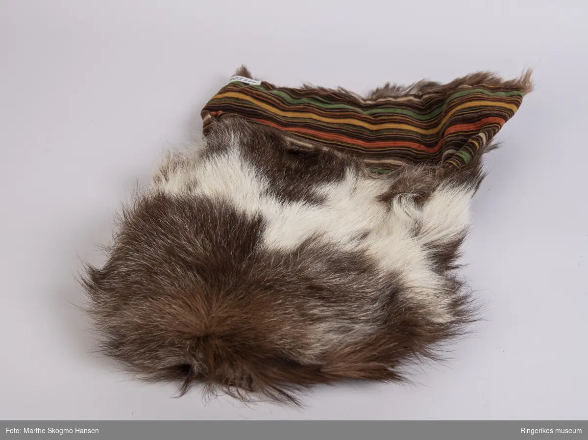 Sovepose til dokker. Posen er sydd av geiteskinn, som er brunt og hvitt. Innvendig er den foret med stripete cordfløyel. Posen ble sydd av Edel Gusgaard (1911-2000).
