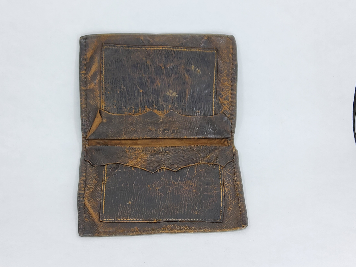 Plånbok av svart läder med flera fack. Ett fack innehåller brev med upplysningar. Tillverkad av givarens morfar 1860.
