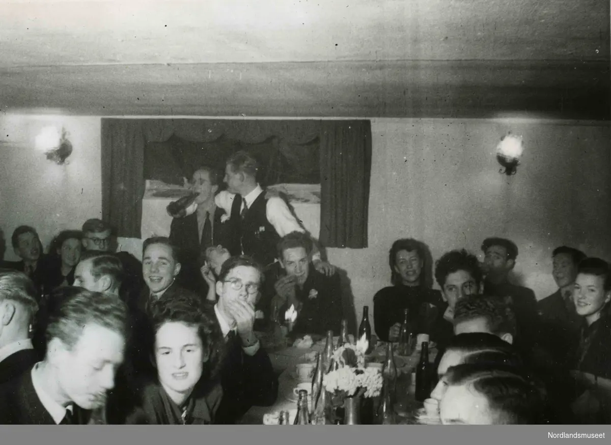 Mange unge mennesker i lystig lag. Bildetekst: Russefest i Ihlenkjelleren. Desember 1943".
