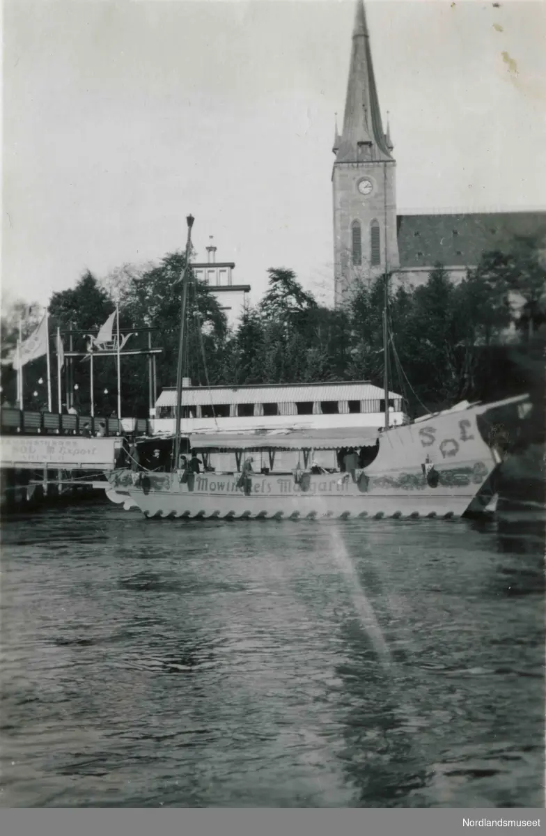 Ilen kirke i Trondheim. En båt med skriften "Mowinckels margarin" i elva i forgrunnen.