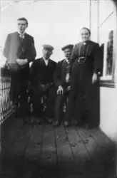 Gruppebilde av tre menn og en kvinne på en veranda.