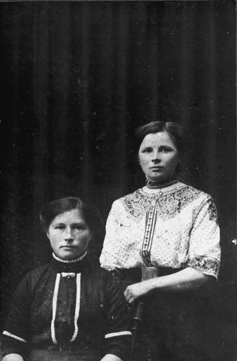 Studioportrett av to kvinner, en sittende og en stående bak.