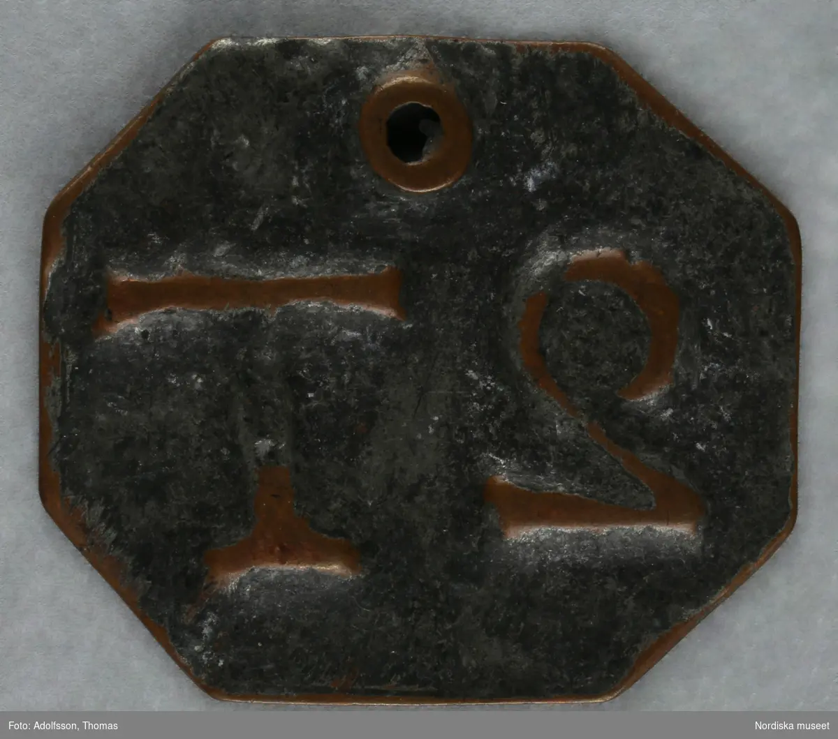 Pollett, av koppar, fyrkantig, hål, präglad text: "2 T".