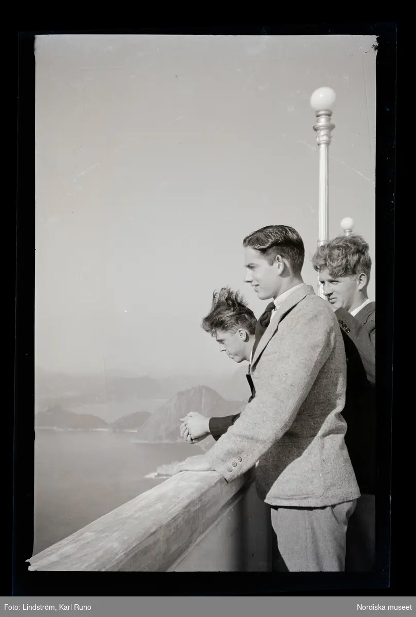 Tre unga män står och betraktar utsikten mot berg och hav.