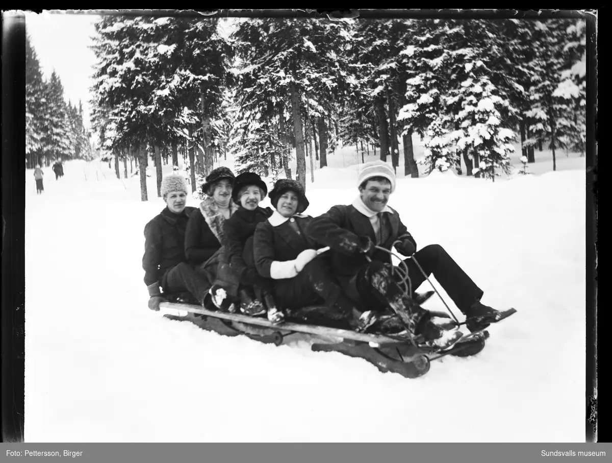 Två män och tre kvinnor åker på en stor kälke i en snöig skogsbacke.