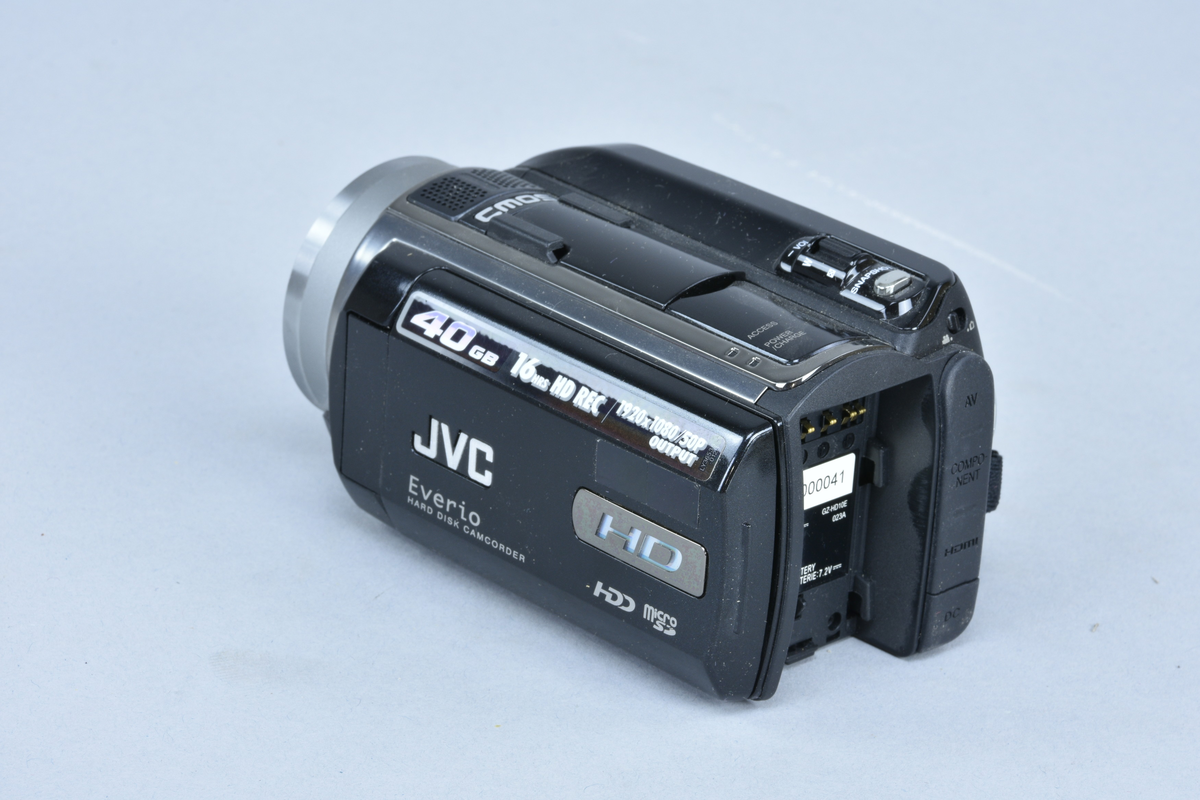 Digital mediakamera med inbyggd stereomikrofon JVC typ GZ-HD10E nr 00000041 (förserieexemplar). För lagring på inbyggd hårddisk och minneskort typ Micro-SD. Zoom och autofokus, 1:1.8 brännvidd 3.2-32 mm från Konika Minolta. Utvikbar display med knappar och joystick. "One touch upload" till Youtube, export eller "Dirct VD". CMOS-teknik. Hårddisken på 40 GB ger 16 timmars HD-inspelning. Plats för batteri 7,2 V samt ingång för nätaggregat.