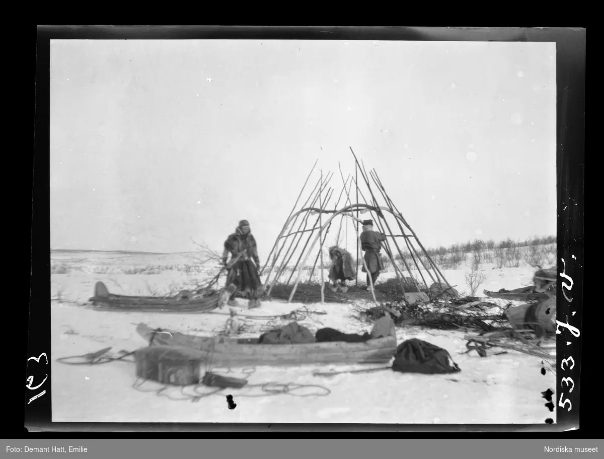 Tre personer, Jouna och Anne Rasti samt deras dotter Marge, har slagit läger och reser en kåta under vårflyttningen från Närvä. Bilden ingår i en serie fotografier tagna av Emilie Demant Hatt i Sapmi mellan åren 1907 och 1916.