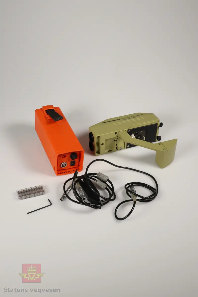 En oransje beholder som inneholder en elektronisk avstandsmåler av typen DISTOMAT WILD DI1600, et eksternt batteri, ti ekstra sikringer, en LEMO kabel og en unbrakonøkkel. 