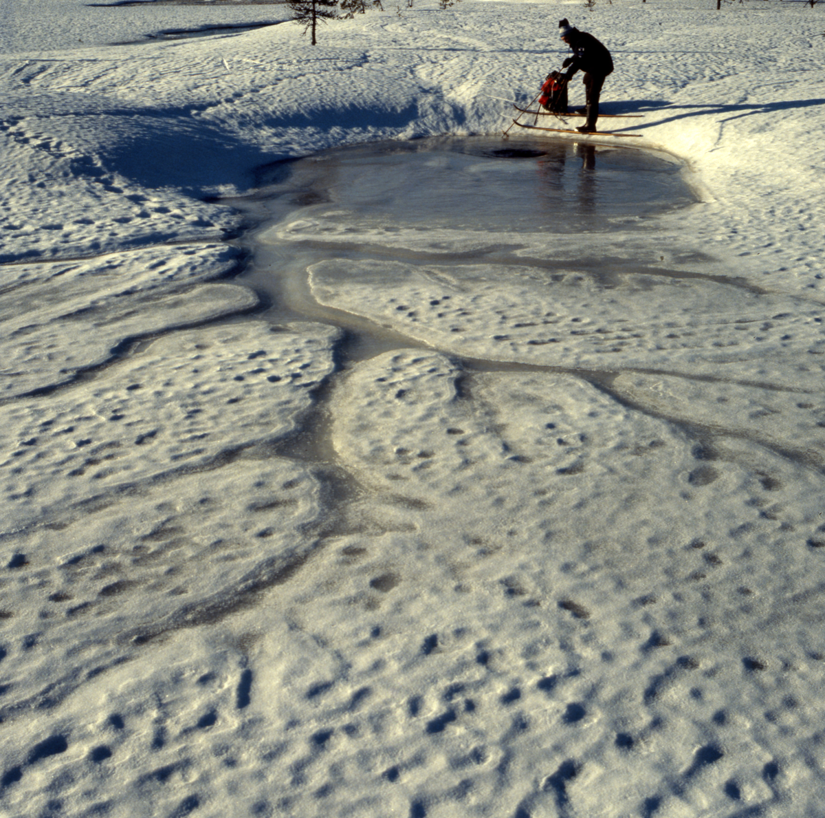 En man på ett par skidor står med sin ryggsäck väldigt nära en isvak.