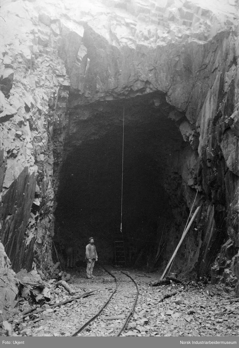 Arbeider stående i tunellåpningen til inntaket ved Skarfoss. Smalsporet jernbanespor ligger innover i tunellen.