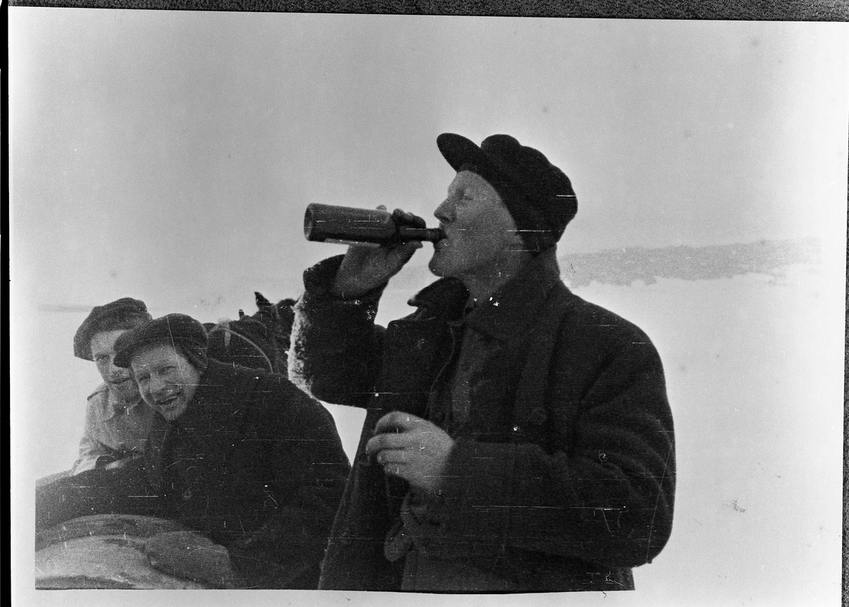 Ett av en serie fotos tatt på hjemtur etter å ha kjørt sprit fra Hjell Brenneri til Hamar.
Sigurd Strand og Pål Taralrud lener seg mot tomtønna og ler til Pål Gjestvang som tar seg en god støyt av flaska.