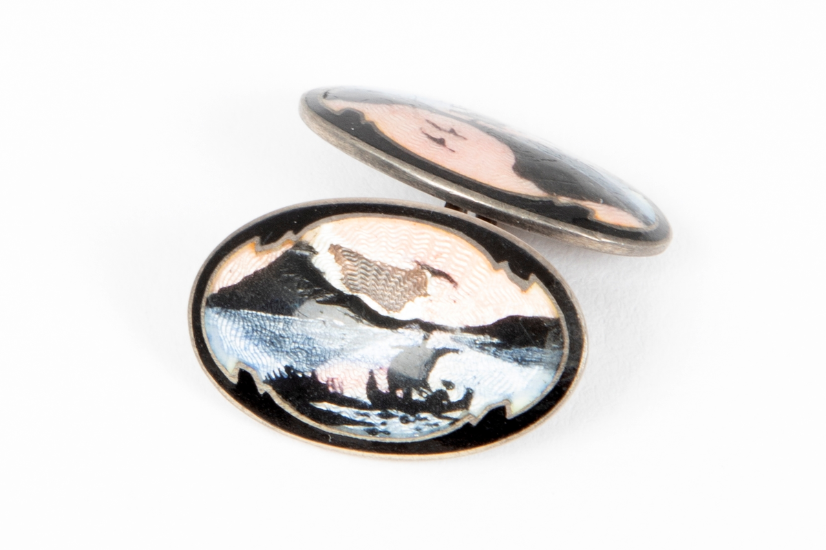 Ovalformet mansjettknapp i sølv med emalje over guillochering. Landskapsmotiv med vikingskip i svart mot rosa og lyseblå bunn.
