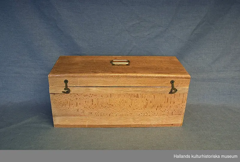 Sjukvårdslåda i trä från tidigt 1900-tal. Lådan innehåller två armbindlar, två mitellor, en leukoplastrulle, kloramintabletter, ask för säkerhetsnålar "The Globe", en glasflaska med natriumbikarbonat, 