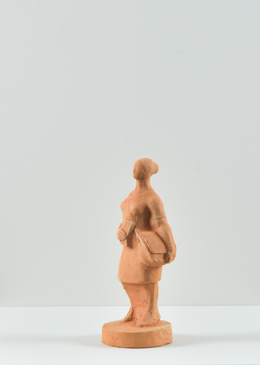 Skulptur på sokkel av en dame med veske og avis. 