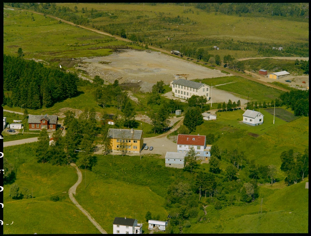 Leirfjord,Leland. Flyfoto fra Leland. Midt på bildet ligger helsehuset (gult bygg). Her var det tannlege, legekontor og dusjer m.m. Den røde bygningen til venstre er den gamle skolen fra 1880-tallet (nå museum). Den nye skolen, hvit bygning i to etasjer ligger øverst mot høyre.