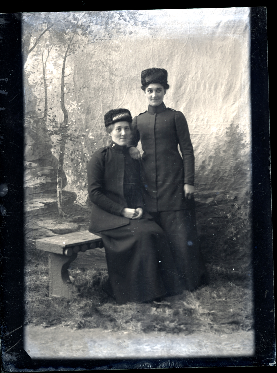 Atelierfoto. To kvinner i Frelsesarmeen uniformer, en eldre kvinne sitter og en yngre kvinne står ved siden.