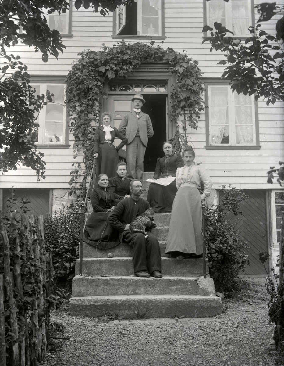 Gruppeportrett av 7 personer på ei trapp foran et hus.