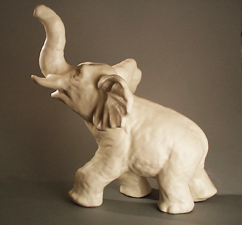 Prydnadsföremål i form av elefant med höjd snabel, av keramik med halvblank vit glasyr, gjuten.

