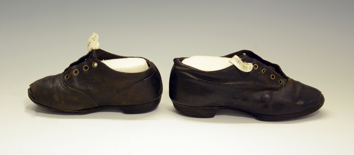 Barnesko. 1 stk sko i brunt lær med 4 stk snørehull med metallmaljer. Jernstifter i hæl og treplugger i sålen.