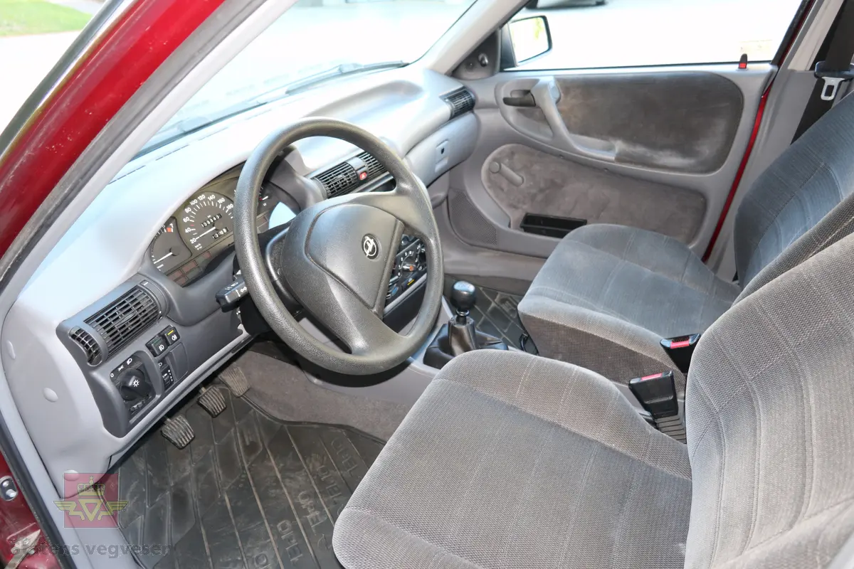 Opel Astra 2.0 I GLS. Rød 4 dørs personbil med 4 hjul og framhjulstrekk. Bilen har en bensindrevet 4-sylindret rekkemotor (forbrenningsmotor) med et sylindervolum på 1998 kubikkcentimeter og en effekt på 85 kW (116 hk). Motorbetegnelsen er C20NE. Girkassen er en 5-trinns manuell type. Bilen fremstår som original og nesten ubrukt med ca. 6000 km på telleren. Den har noen små sår i lakken og har aldri vært omlakkert. Lakk/trimkode er E-549 - 151. Dekk foran og bak skal være 175/65 R 14. Fem sitteplasser.