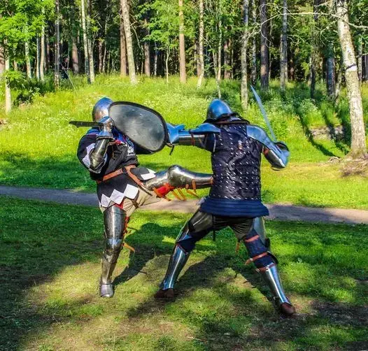 To riddere i platerustning med sverd, skjold og skaberakker i hvit og svart med nagler. De sloss og den ene sparker den andre,