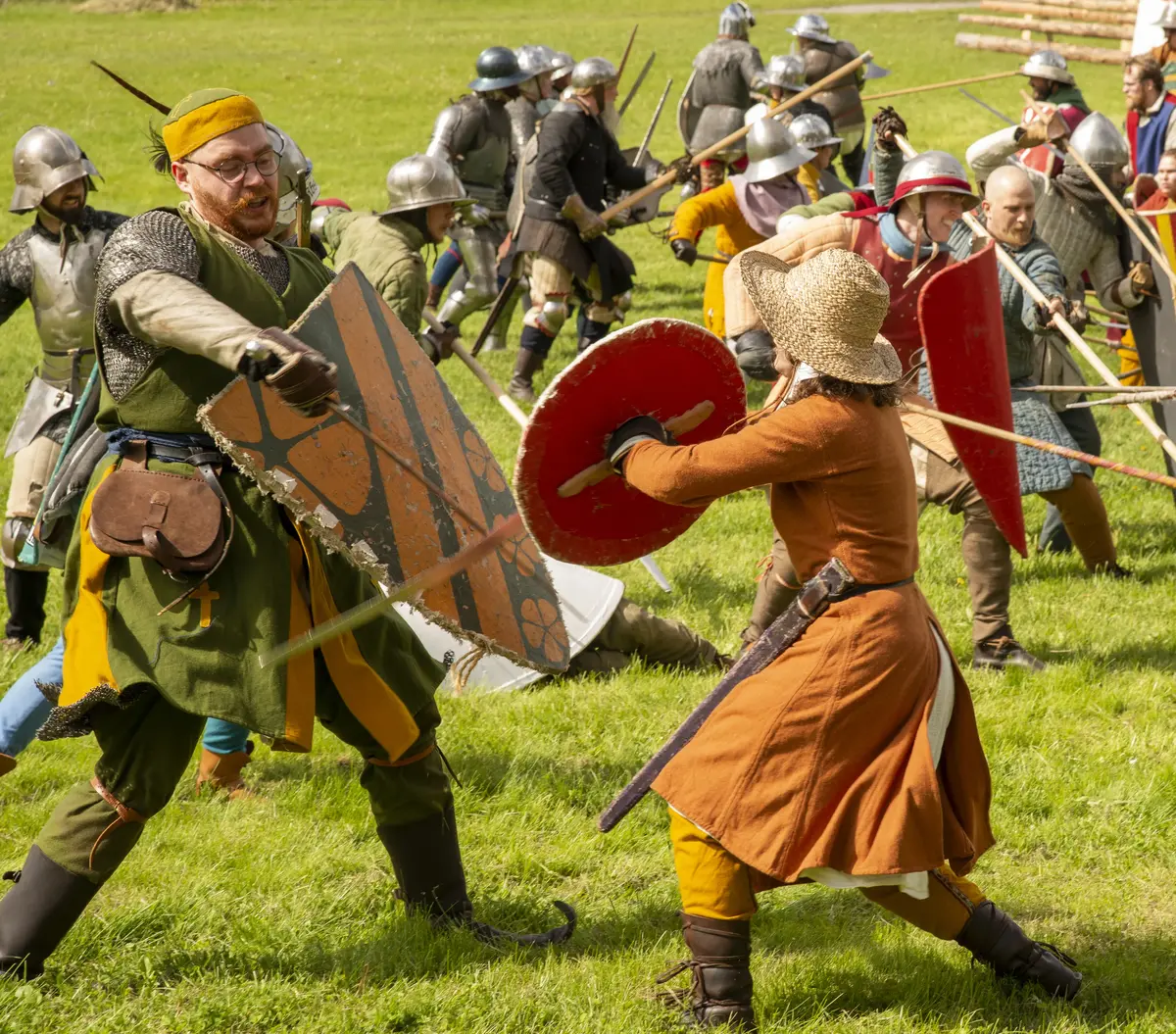 Two warriors in medieval costumes fighting with swords and shields.