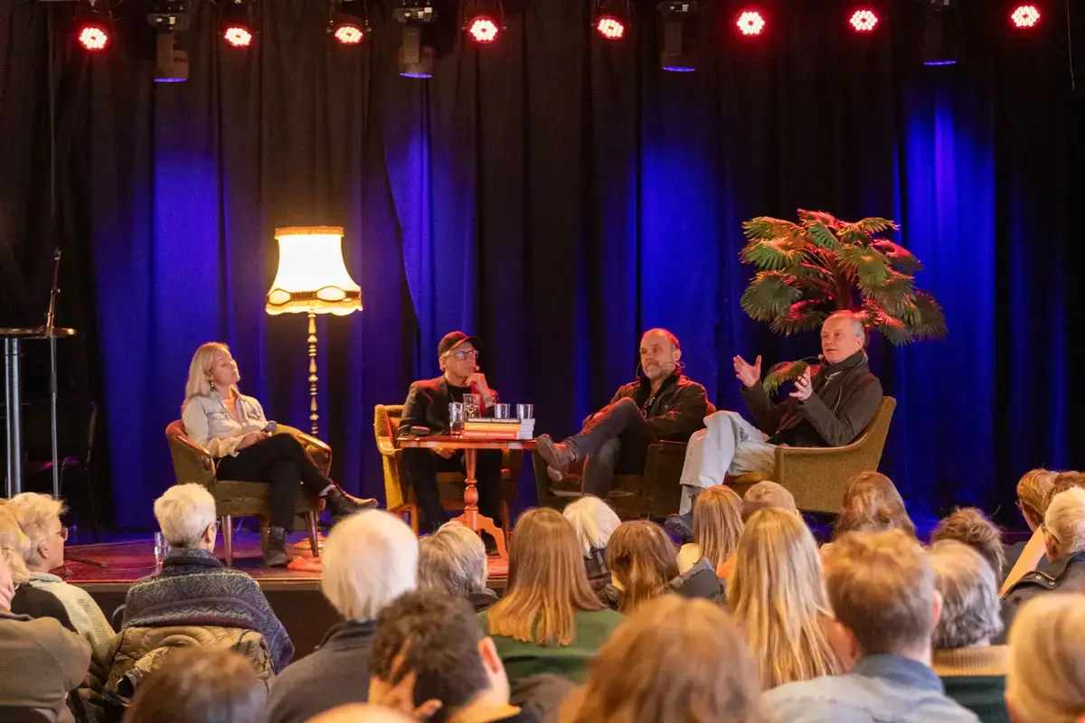 Fire personer sitter på en scene og snakker foran publikummere.
