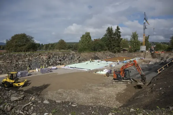 Oversiktsbilde som viser litt av størrelsen på grunnflata til Regionalt Historiesenter: nede i hullet til bygget står en gul veivals og ei oransje gravemaskin i tillegg til bittesmå arbeidere som legger markisolasjon og armeringsjern, med heisekrana i bakgrunnen.