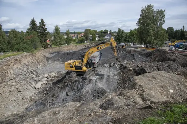 En oransje gravemaskin står midt i et stort hull.