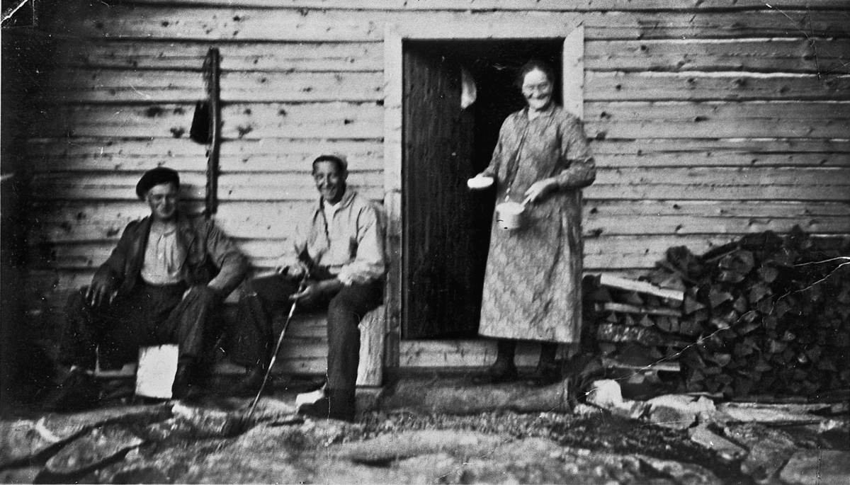 Kvinne og 2 menn utenfor et tømmerhus.