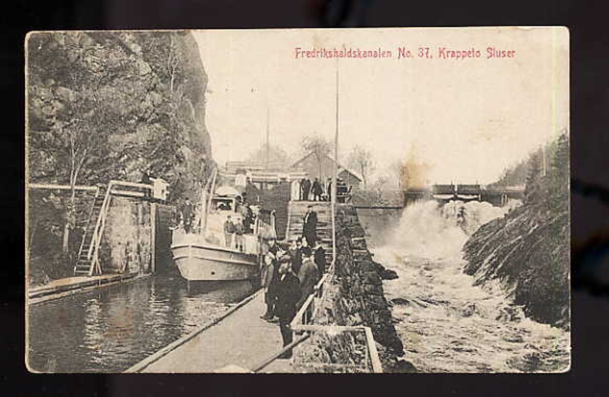 Urskog-Hølandsbanens motorbåt M/B Njord  i Krappeto sluser i Fredrikshaldskanalen. Postkort nr. 37 utgitt av M. Olsens papirhandel i Fredrikshald (Halden). Sommerrute for M/B Njord for 1911.