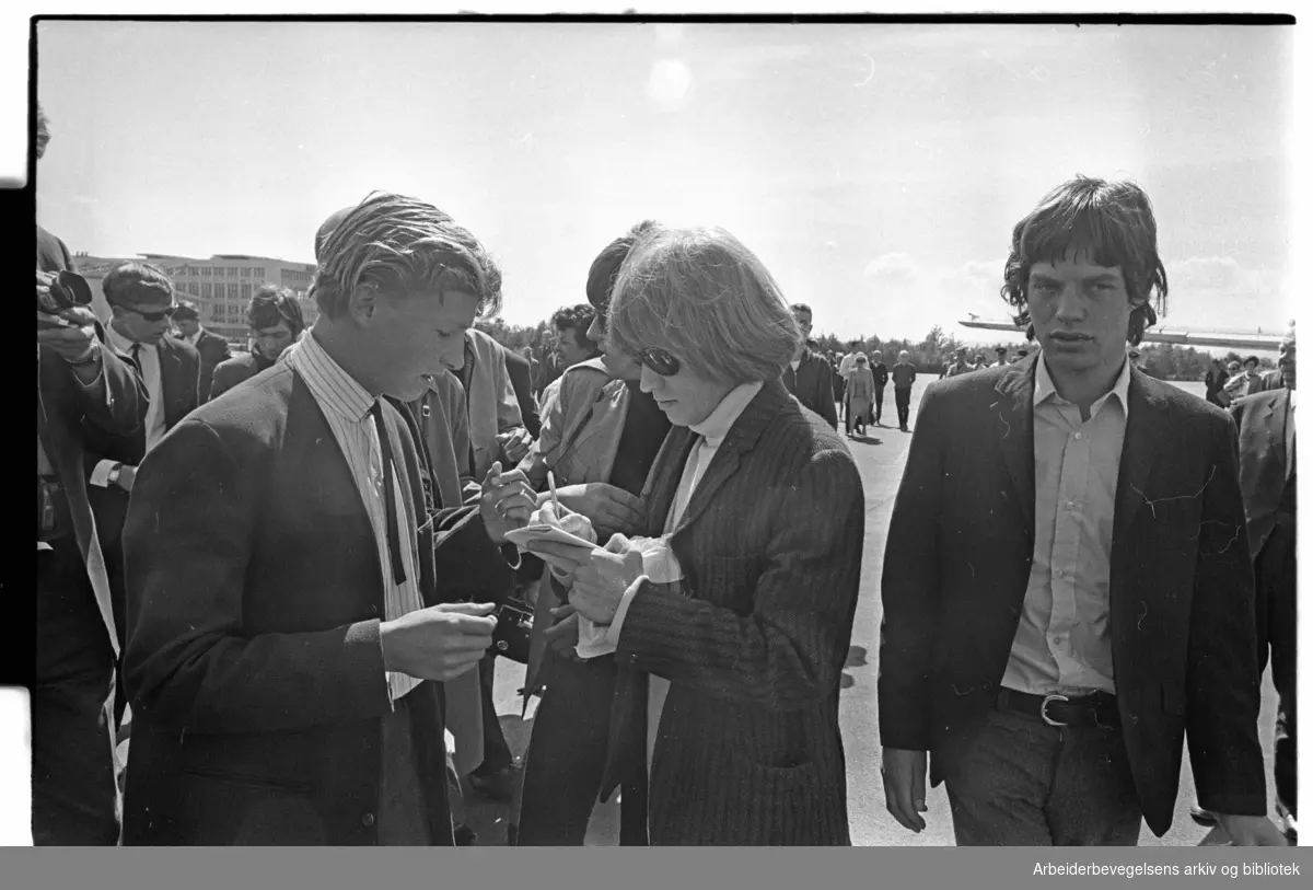 The Rolling Stones ankommer Oslo, via Fornebu flyplass, 23. juni 1965. .Brian Jones skriver autografer. Mick Jagger til høyre..