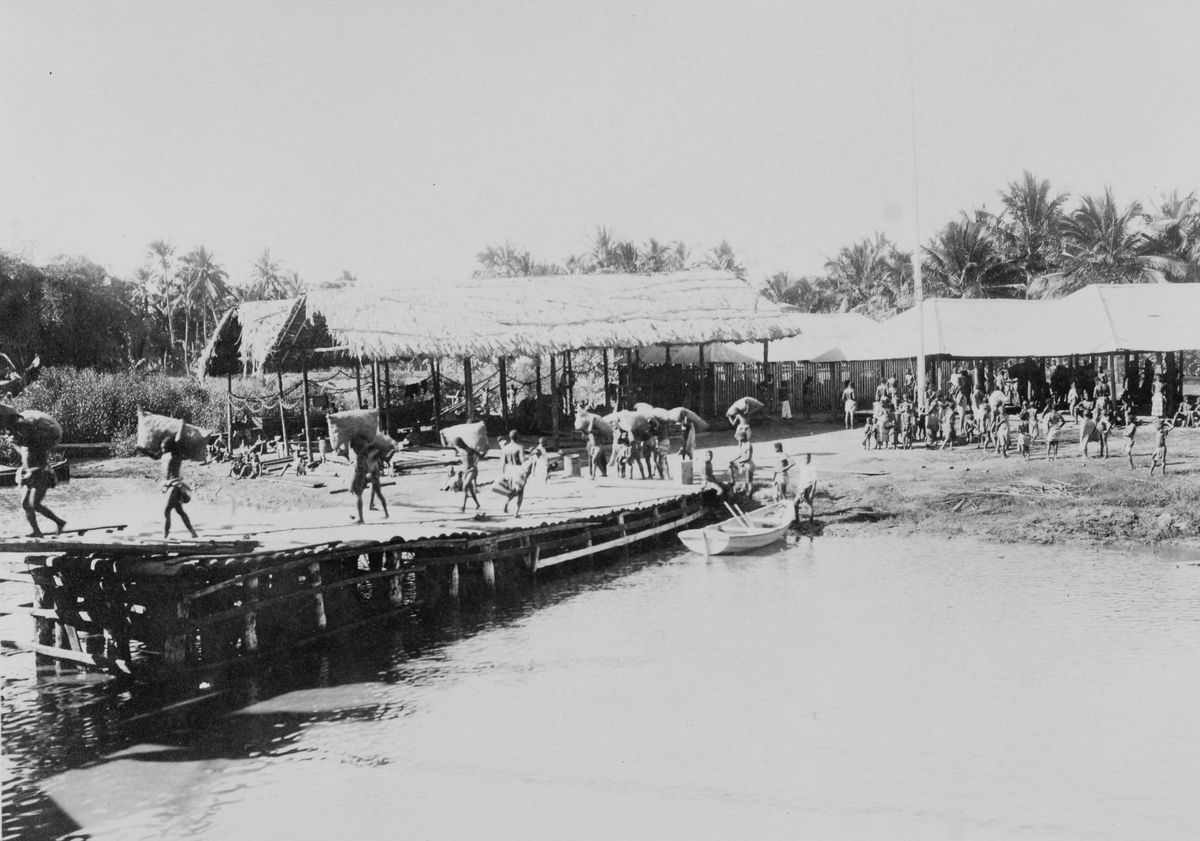 Mosambik. 1914. Sekker med kopra bæres på en brygge ut til lasteskipet.