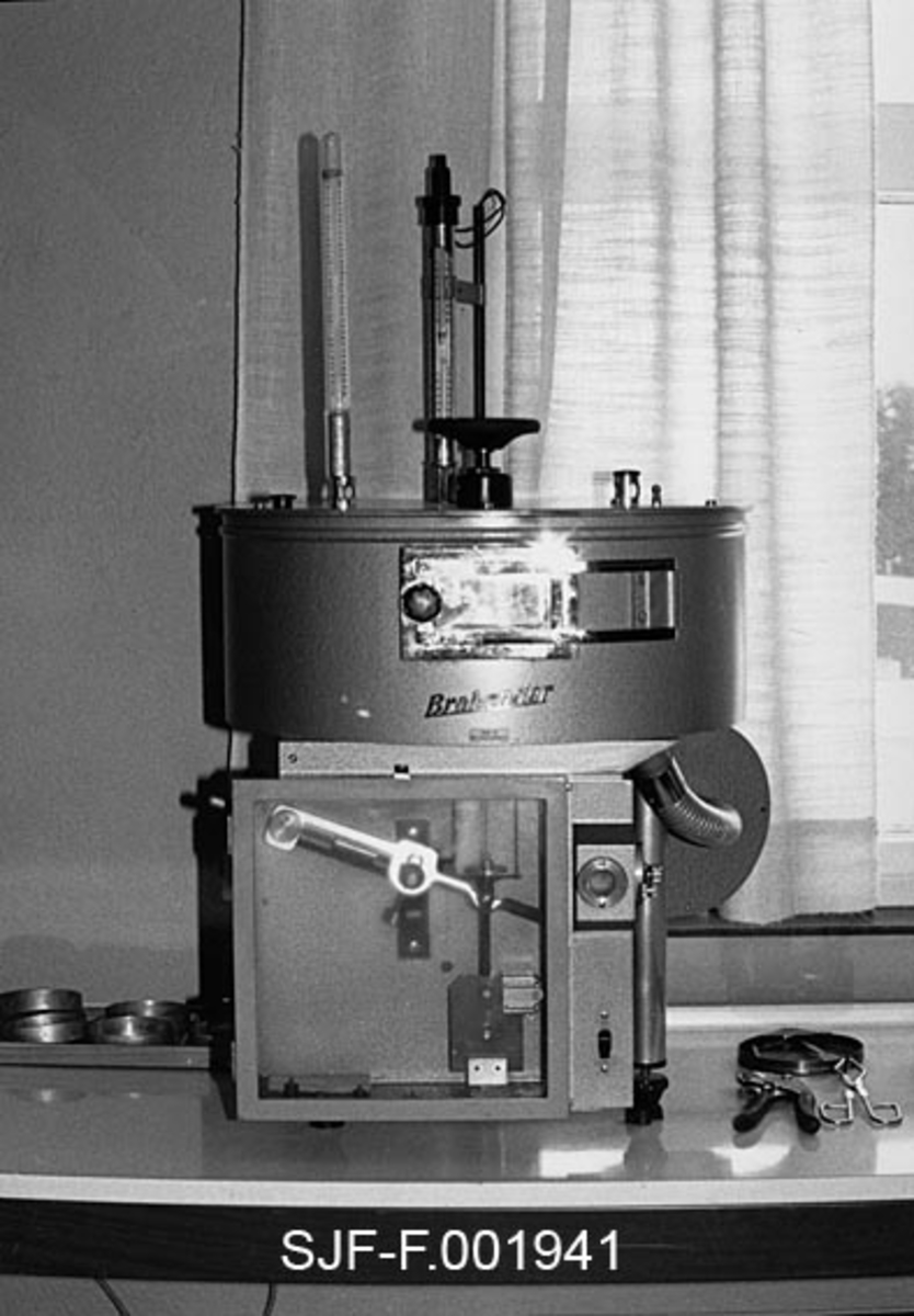 Såkalt "Brahbender" fra laboratoriet ved Skogfrøverket på Hamar.  Brahbenderen ble brukt til måling av fuktigheten i frøet.  Maskinen målte vekktap etter en tørkeprosess.  Fotografiet er tatt i 1981. 