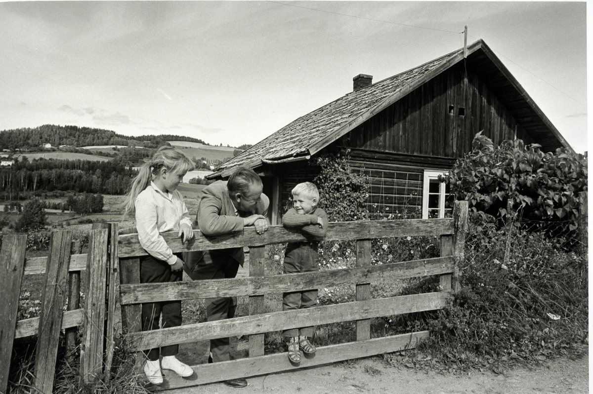 Alf Prøysen i Ringsaker i 1961, foto Johan Brun for Dagbladet, negativer på Hedmarksmuseet. 
ALF PRØYSEN, 2 BARN: MARY KRISTINE OG JAN OLAF HAGEN, GRINDA FORAN PRØYSENSTUA, RINGSAKER. FOTO: JOHAN BRUN, 1961
