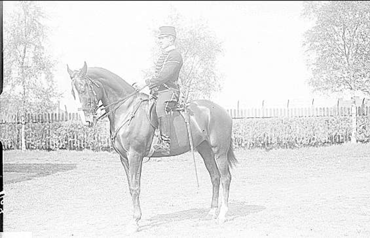 Korpral (hästskötare) i uniform m/1895 med oficers tjänstehäst på kasernområdets norra del, vid staketet mot Volvo - Pentaverken.