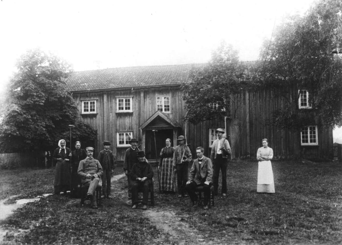 Nordre Asak, Sørum, Akershus ca. 1890-årene. Bildet viser den gamle hovedbygningen på Nordre Asak, mennesker samlet for fotografering foran huset. Noen sittende og noen med river.