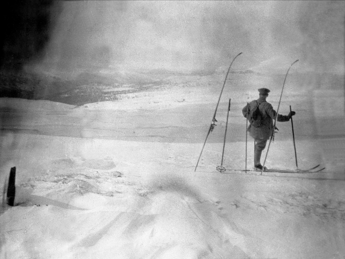 En mann er på står å ser utover en vidde med ski på beina. Robsahm og Lund.