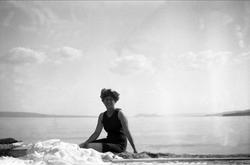 En kvinne med badedrakt sitter å poserer på stranden. Robsah