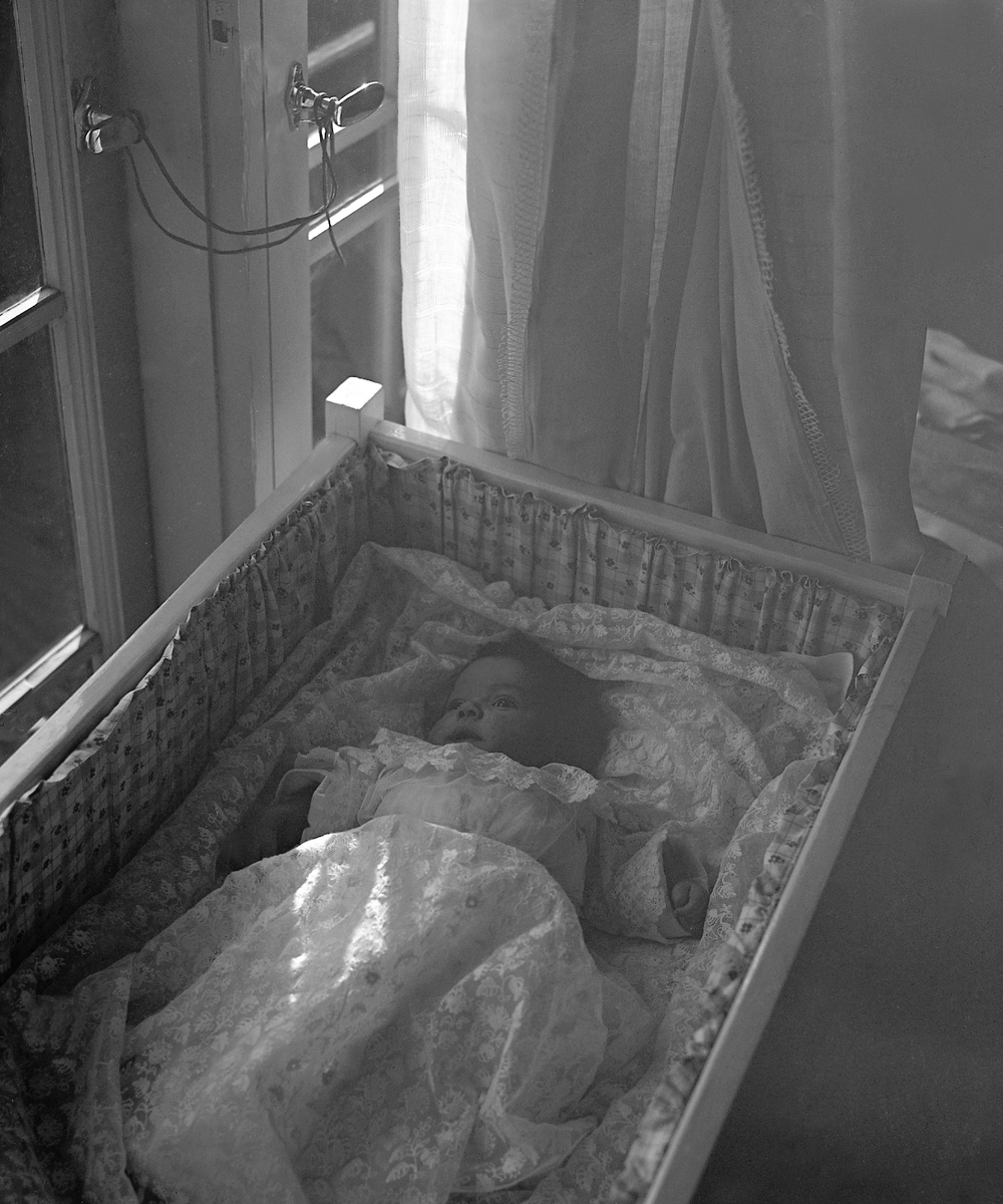 Dåpsbarnet Kari Arentz ligger i sengen med dåpskjole. Fotografert 8. september 1935.