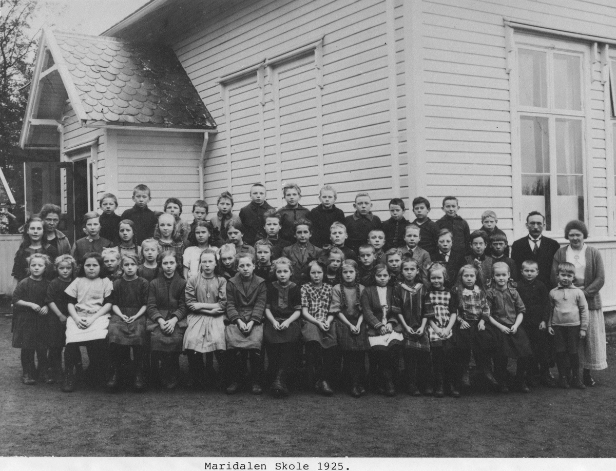 Gruppebilde av elever ved Maridalen skole, Oslo, 1925. Elevene er plassert i 3 rader foran skolebygningen med lærer Kristian Halsnes på høyre side.